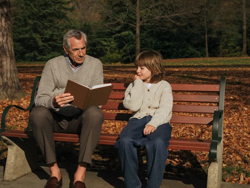 Un grand-père et son petit-fils lisent ensemble un carnet sur un banc de parc.